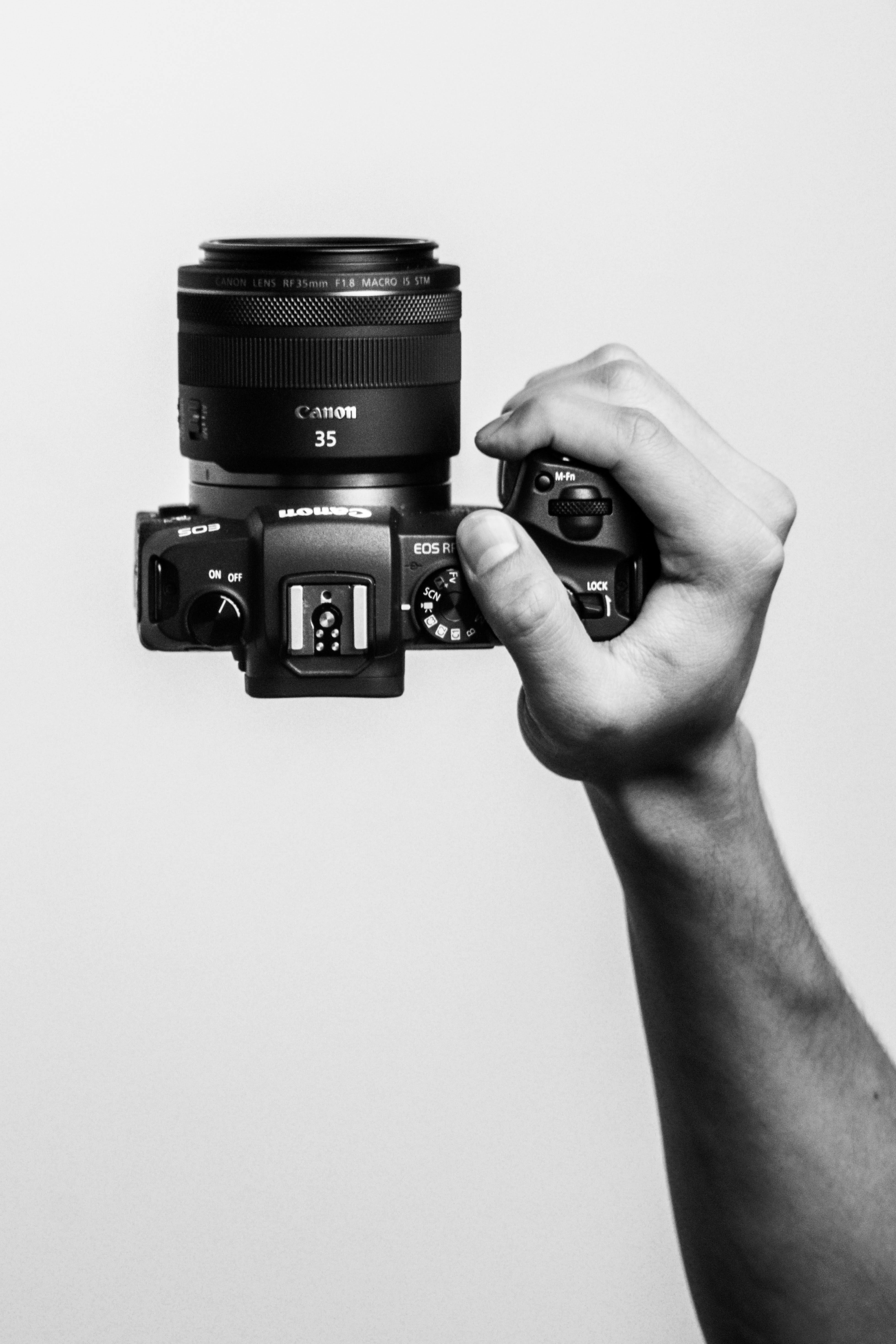 Bir el, beyaz arka planda Canon EOS R6 kamera tutuyor.